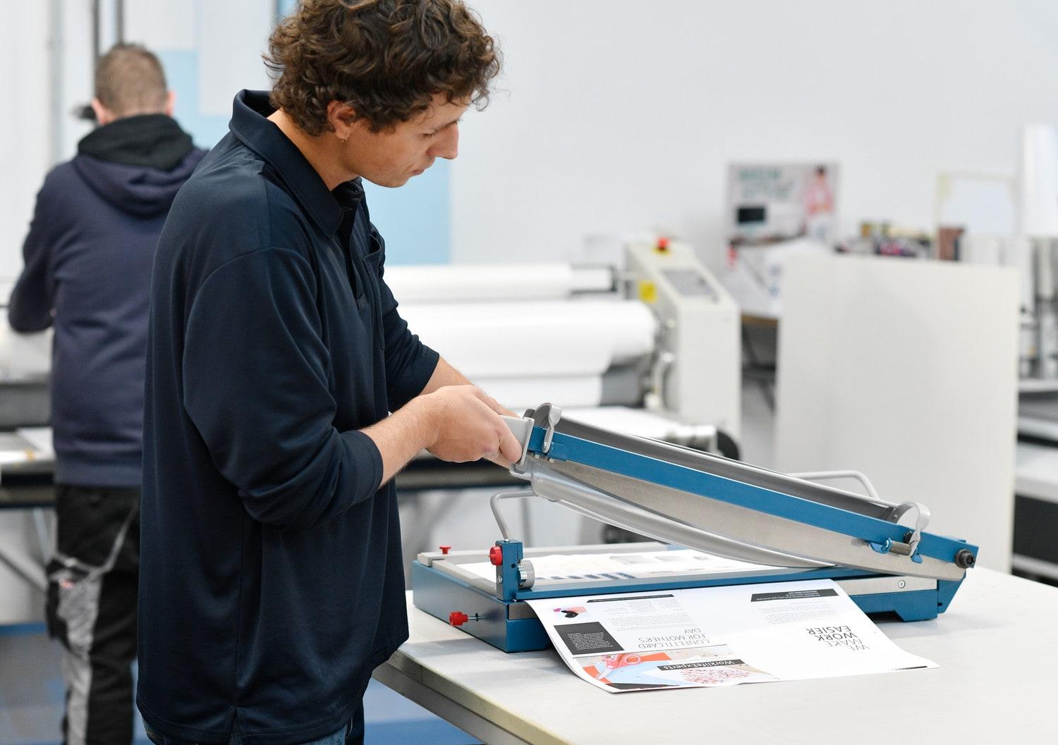 Découpe d'une feuille sur une cisaille grand format dans un atelier d'impression
